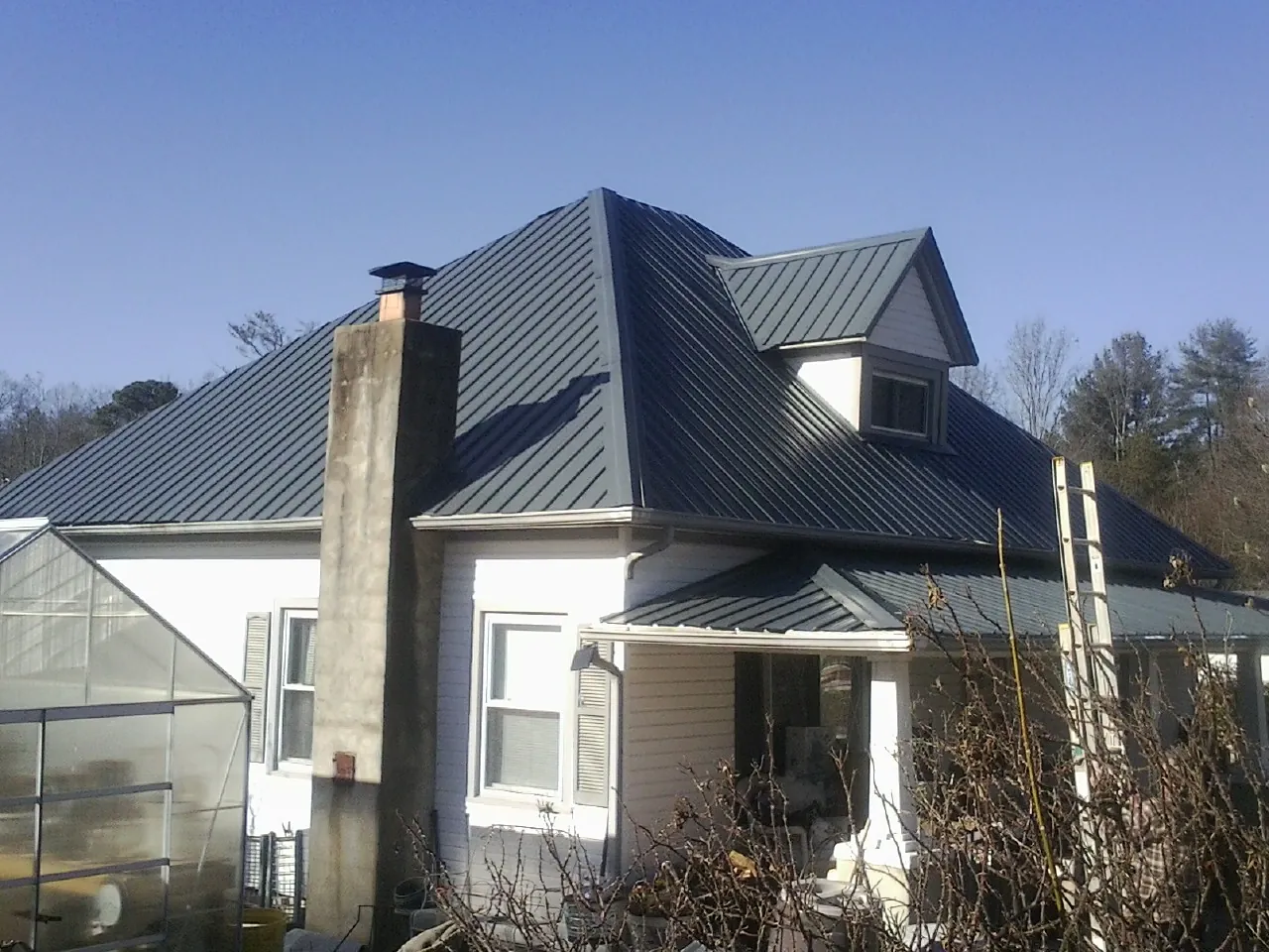 Dark blue standing seam metal roof on a white farmhouse with dormer — Slate & Tile Roof Repair by Roofing Brothers in Lockwood