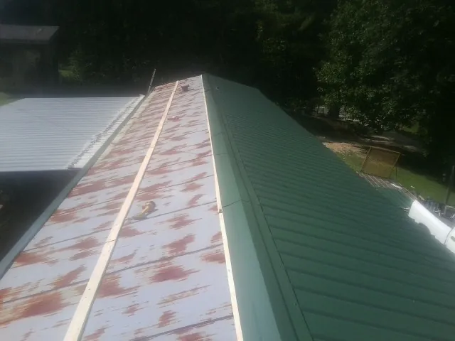Old rusted panels beside newly installed green metal roofing — Wind Damage Roof Repair by Roofing Brothers in Lockwood