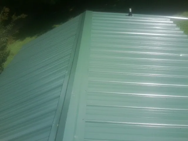 New green metal panels meeting at the ridge of a roof — Flat Roof Repair work by our crew in Lockwood